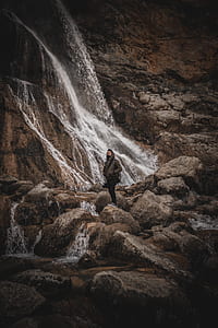 photo of man wearing brown jacket near waterfalls thumbnail