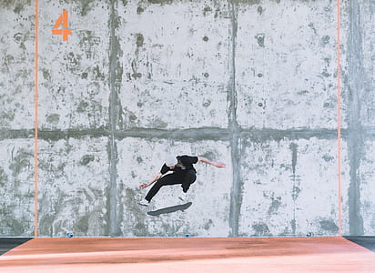 man riding on skateboard jumping on brown surface near gray concrete wall at daytime thumbnail