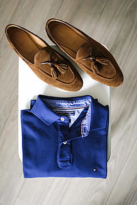 pair of brown suede tasseled loafers beside blue polo shirt on white pavement thumbnail