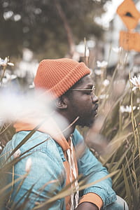 man wearing blue denim jacket and orange knit cap sitting in the middle of white petaled flower thumbnail