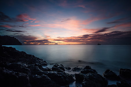 rock formation beside body of water during sunset thumbnail