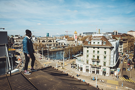 person standing on top of brown roof facing city buildings at daytime thumbnail