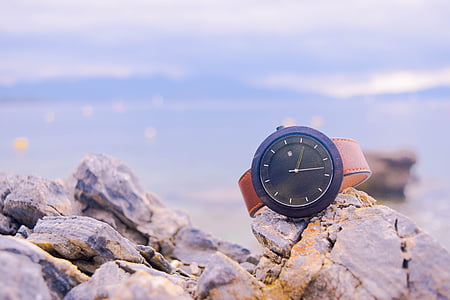 round black Movado analog watch with brown leather strap on grey and brown stone thumbnail