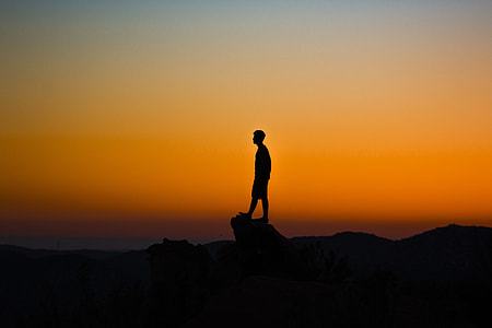 silhouette of man standing on rock cliff thumbnail