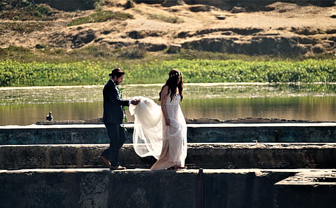 man and woman walking on gray concrete railing near body of water thumbnail