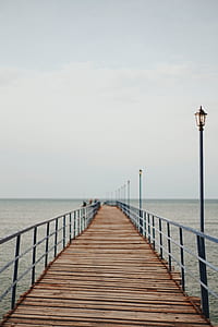 wooden dock with street lights over body of water under cloudy sky thumbnail