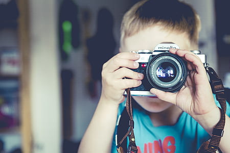 selective focus photography of boy wearing blue crew-neck shirt using black and grey camera thumbnail