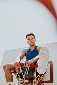 man in blue tank top sitting on basketball ring thumbnail