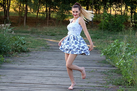 woman wearing white and blue floral square-neckline mini dress walking on gray pallet pathway with barefoot thumbnail