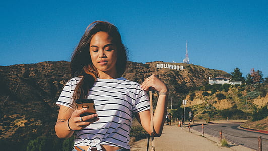 woman in white and black striped scoop-neck top standing near Hollywood sign thumbnail