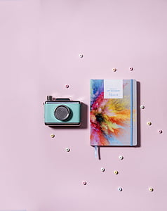 teal and silver-colored MILC camera beside paint powder burst book cover on pink surface thumbnail