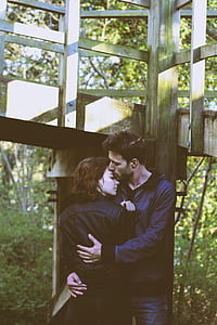 man embracing woman standing under gray wooden bridge during daytime thumbnail