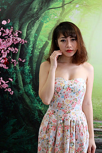 woman wearing white and multicolored floral strapless dress while standing near green tree wall painting thumbnail