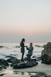 man proposing to woman on rock at the seashore under gray sky thumbnail