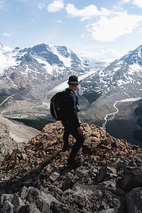 man wearing black sweatshirt and carrying backpack on cliff in front of mountain thumbnail
