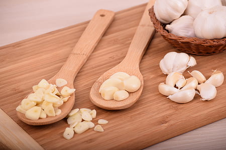 sliced garlic cloves placed on two wooden ladles and chopping board thumbnail