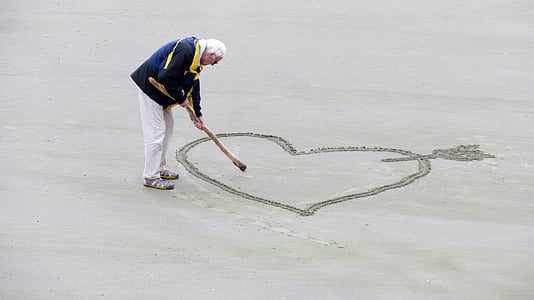 man sketching heart with arrow on sand \ thumbnail