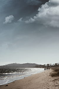 people walking on seashore under gray sky during daytime thumbnail