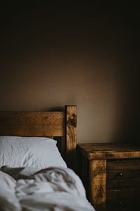 brown wooden bed with white bedspread inside dim light room thumbnail