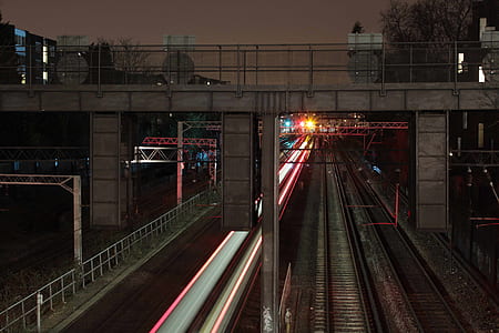 timelapse photography of train passing under foot bridge at night time thumbnail