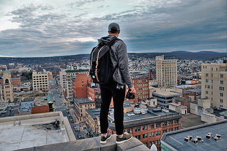 man with black backpack standing on edge of building under cloudy sky during daytime thumbnail