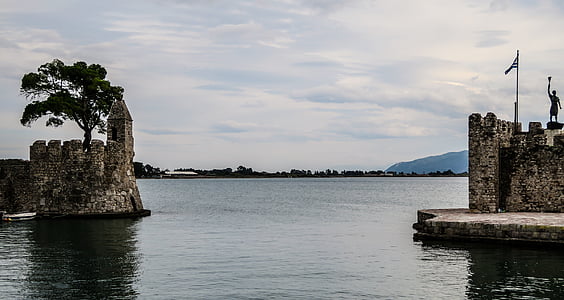 wall castle with statuette near tree and calm body of water at daytime thumbnail
