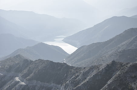 photo of body of water between mountains during foggy daytime thumbnail