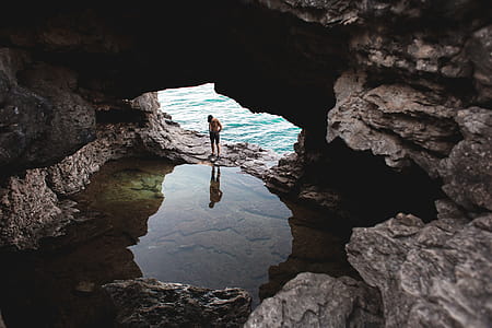 An explorer looks at his reflection in still water in an open cave near a body of water thumbnail