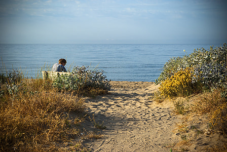 person sitting on sand near body of water thumbnail