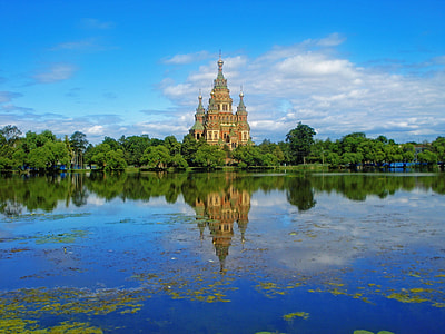 brown concrete castle near green trees with reflection on water under blue and white sky thumbnail