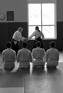 grayscale photo of man holding man's hand in front of four men on floor inside room thumbnail