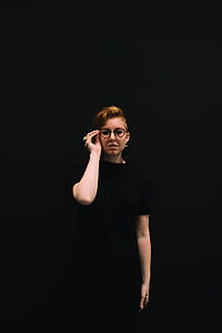 woman wearing black shirt and eyeglasses standing near black backdrop thumbnail
