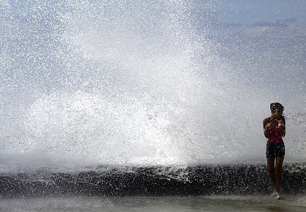 woman wearing red top and blue shorts standing on sea shore with sea waves on her thumbnail