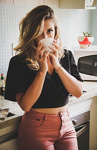 woman sipping from white ceramic mug standing in front of kitchen sink inside kitchen room thumbnail