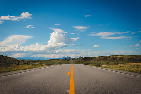 empty concrete road between grass field under blue and white skies thumbnail