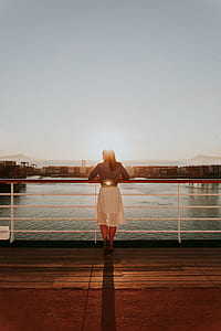 woman leaning on railings near body of water during sunset thumbnail