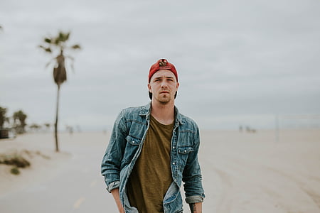 man wearing denim jacket and red cap walking along road thumbnail