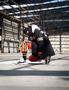 man sitting on floor wearing black jacket and orange pants thumbnail