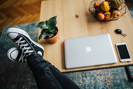 Woman in ripped jeans and black sneakers with a silver laptop on a wooden table thumbnail