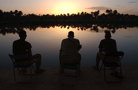 silhouette of three men sitting on chairs in front body of water thumbnail