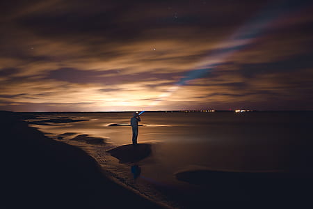 person standing on shoreline holding flashlight pointing upwards thumbnail