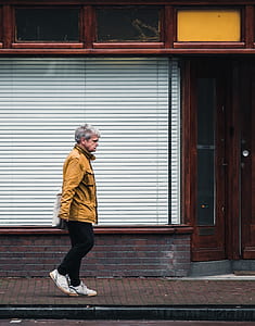 man walking in sidewalk beside white window blinds thumbnail