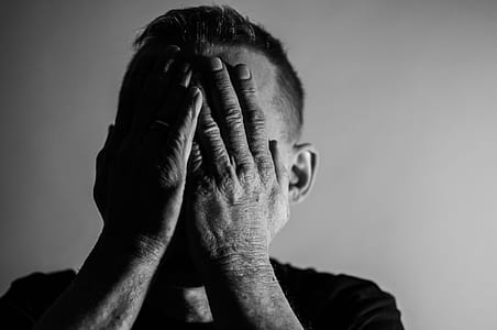 grayscale photo of a man covering his face with both hands thumbnail