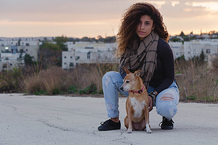 selective focus photography of woman in black long-sleeved top and distressed jeans beside brown dog thumbnail