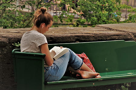 woman in blue denim pants reading book on green bench during daytime thumbnail