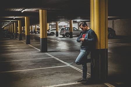 Man in Dark-gray Crew-neck Sweater Standing Leaning to Post in Parking Lot thumbnail