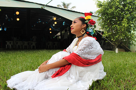 woman wearing white dress with red scarf sitting on grass during daytime thumbnail