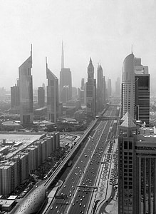 grayscale photography of vehicles travelling on road near buildings thumbnail
