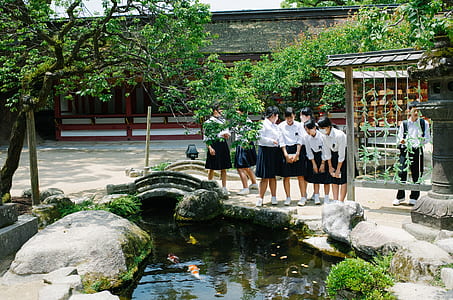 group of students standing beside pond during daytime thumbnail