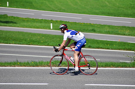 man riding road bike on gray road near grass field thumbnail